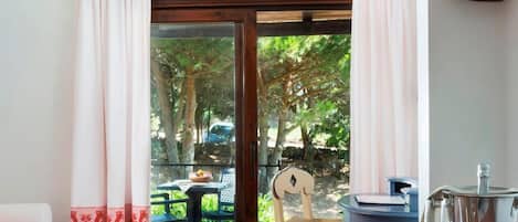 A room with a wooden table, a chair, a sofa, and a view of an outdoor area with trees and a car.