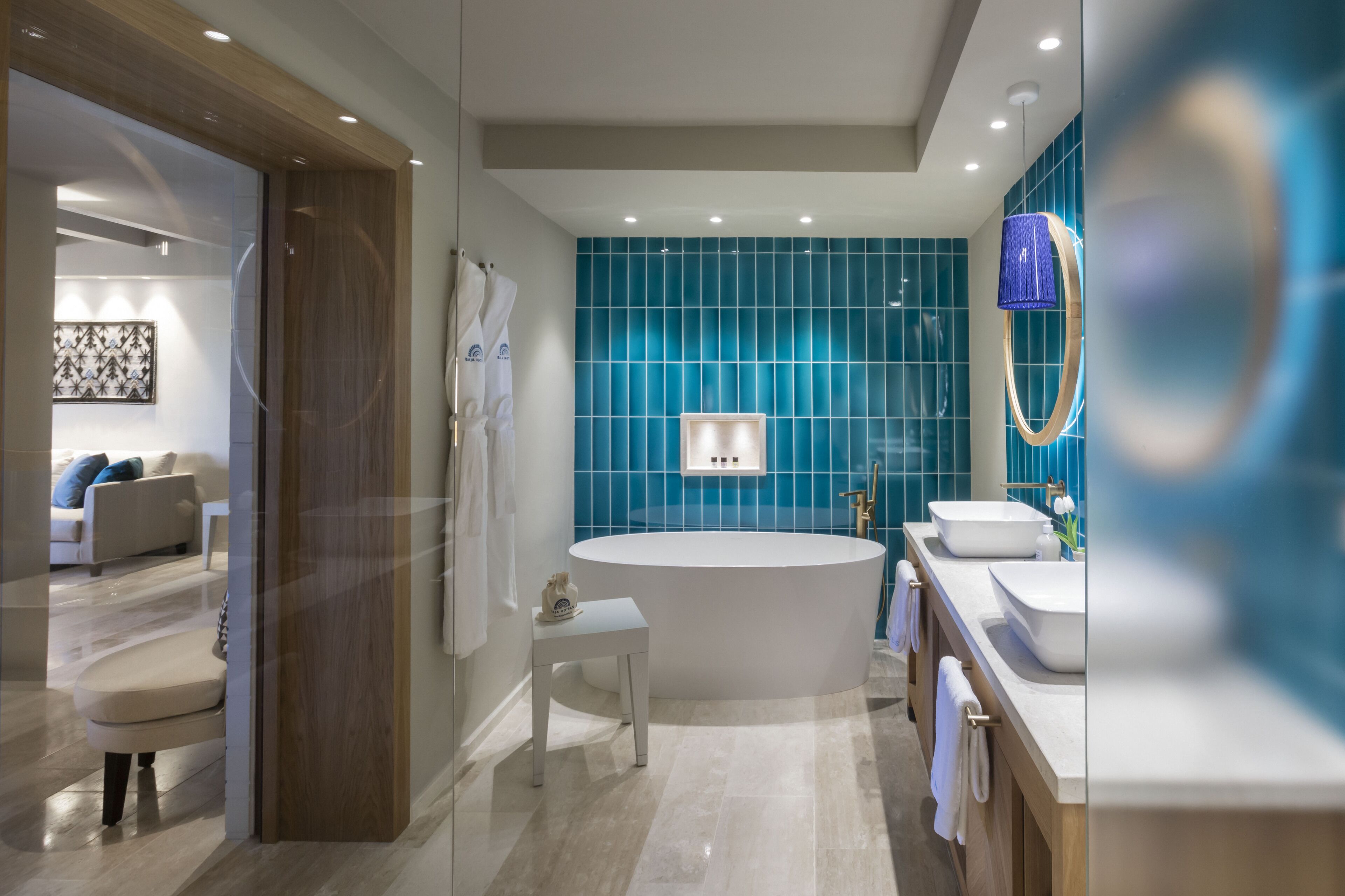 A modern bathroom with a freestanding bathtub, a vanity with two sinks, and a blue-tiled wall.
