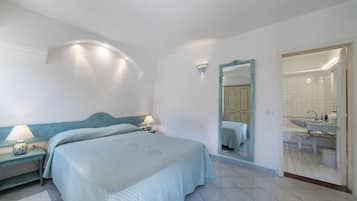 Un dormitorio con cama, mesitas de noche, un espejo y un baño visible a través de una puerta abierta.