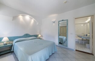 Un dormitorio con cama, mesitas de noche, un espejo y un baño visible a través de una puerta abierta.