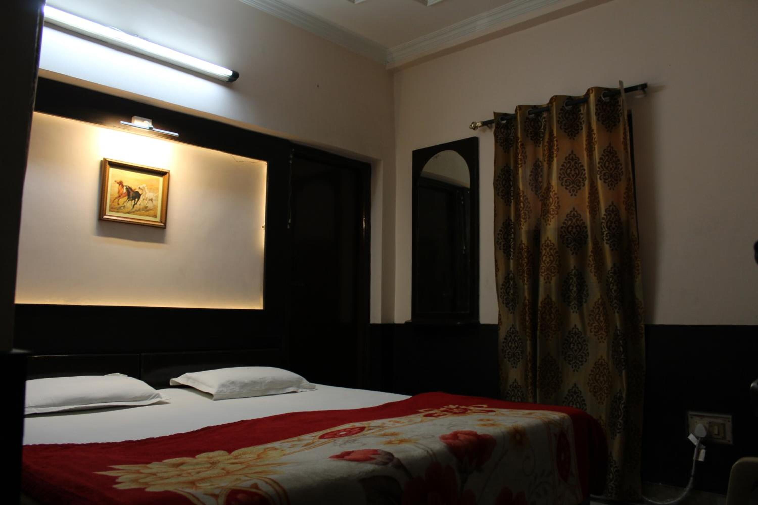 A hotel room with a bed, a painting on the wall, a mirror, and a curtain.