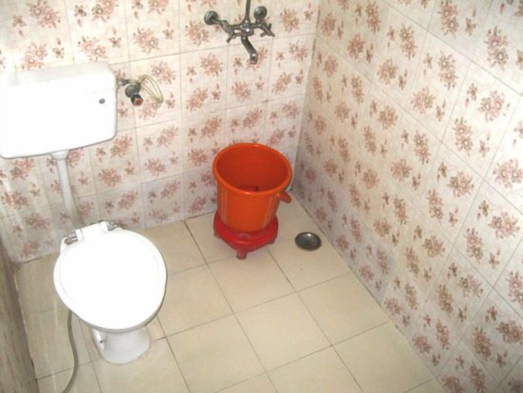 A small bathroom with a toilet, a red bucket, and a showerhead.
