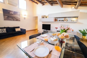 A modern living room with a sofa, a dining table set with plates, glasses, and pastries, and a flat-screen TV. - Splendor Suite Rome - Suites and Apartments (Rome)