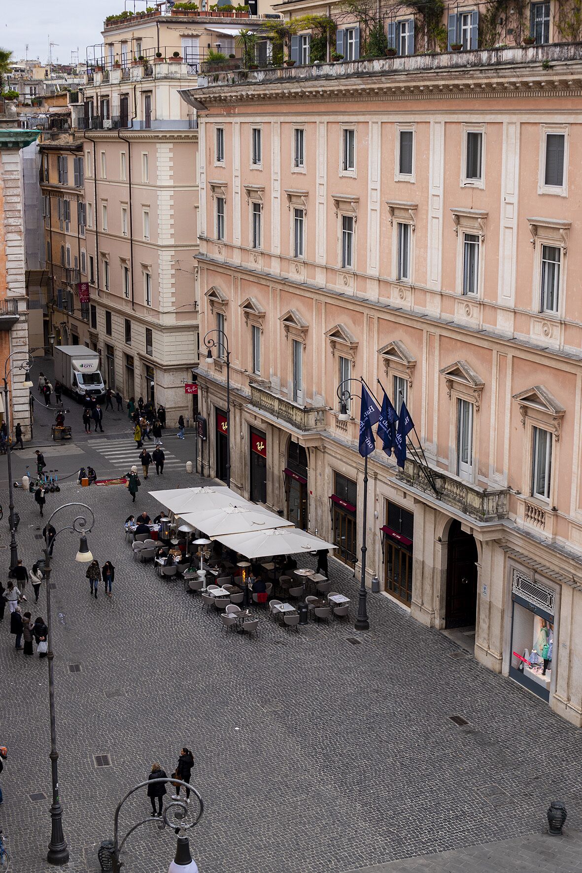 A cobblestone square with outdoor seating, historic buildings, and flags.