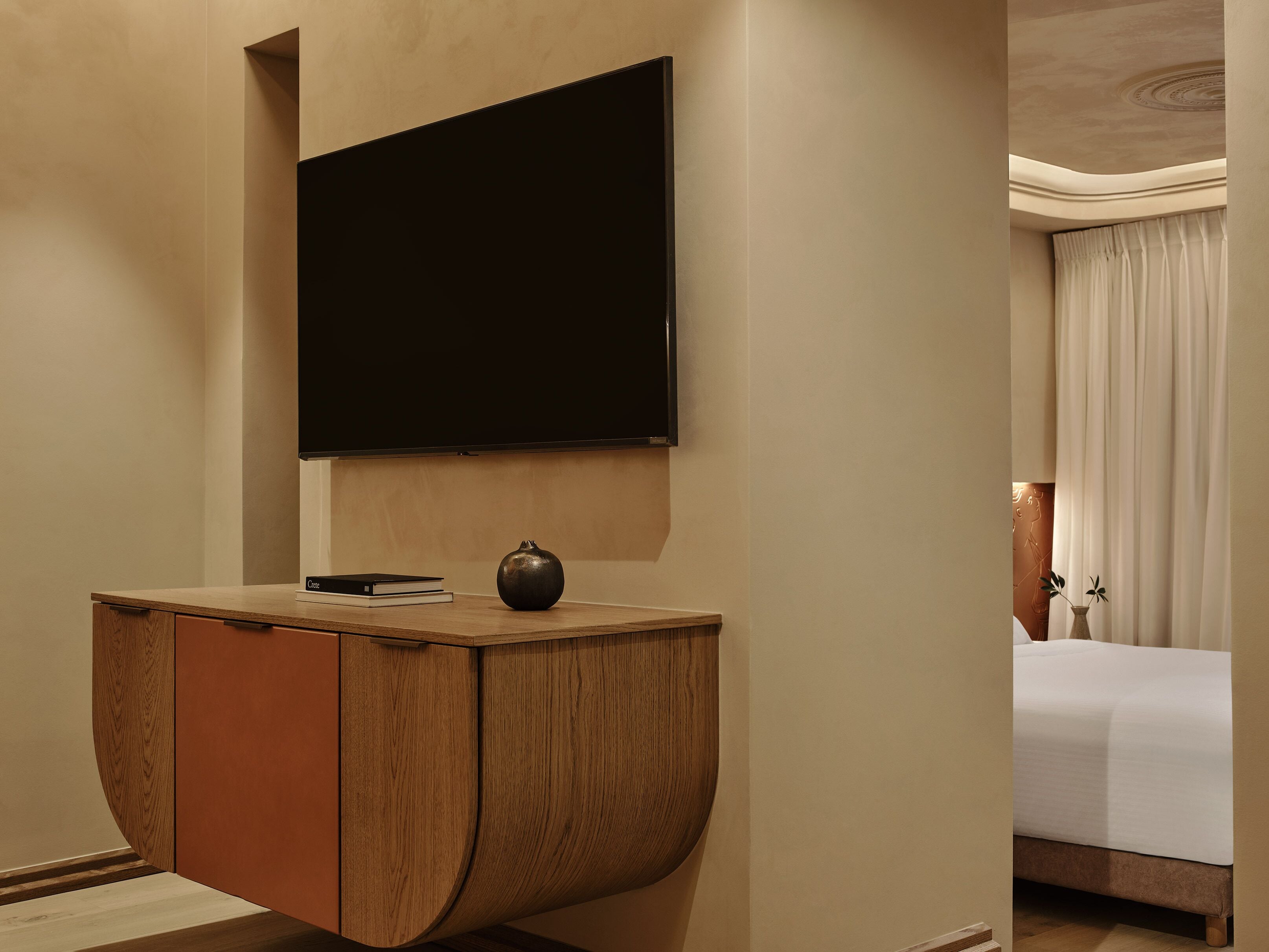 Une chambre d’hôtel dotée d’un téléviseur à écran plat fixé au mur, d’une coiffeuse en bois agrémentée d’un vase et d’un lit à baldaquin.