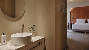 A bathroom with a round mirror, a white sink, a small plant, and a bottle of liquid soap.