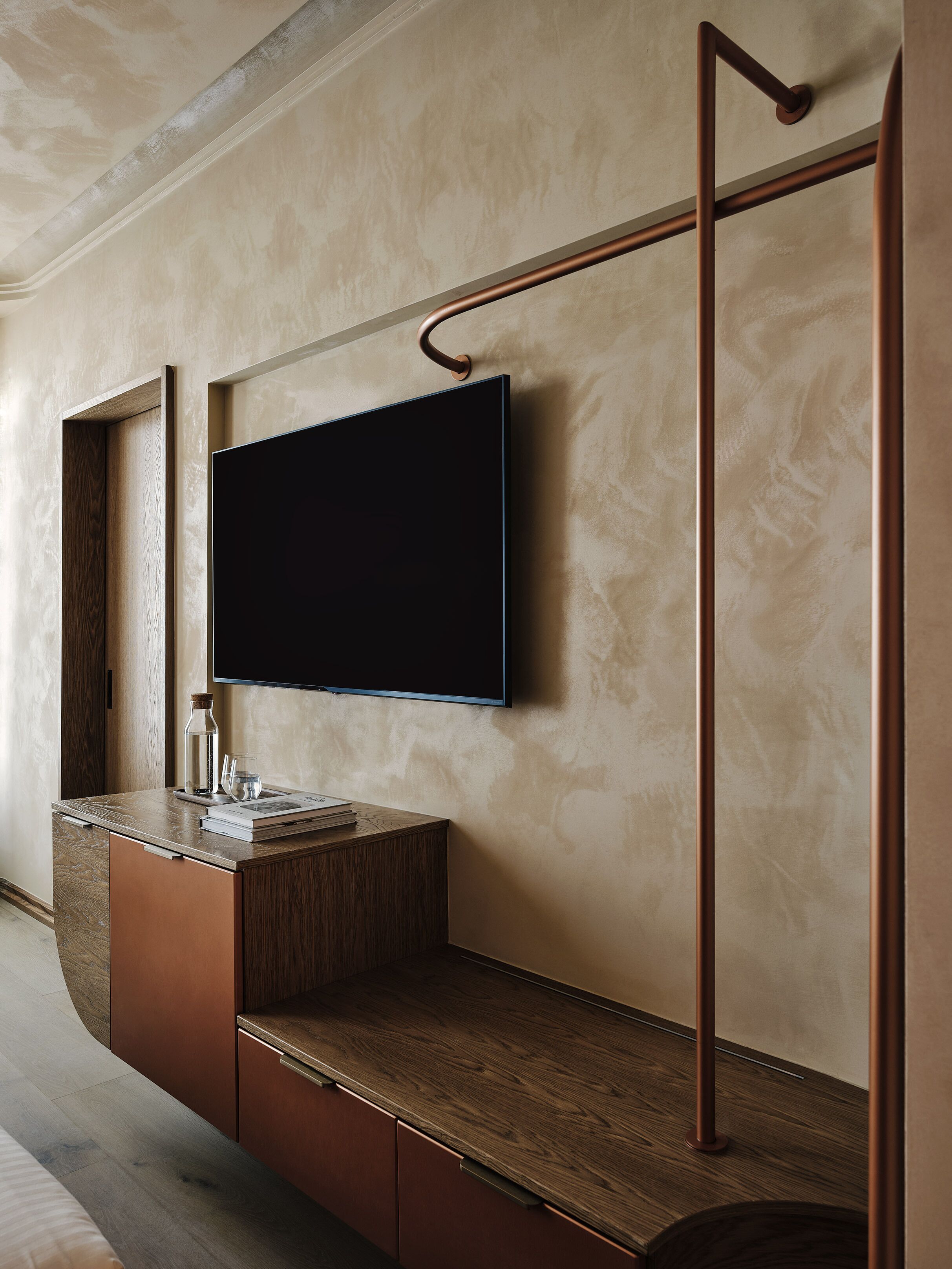 Een moderne badkamer met een houten wastafelmeubel, een spiegel, een flatscreen televisie en een handdoekhouder.