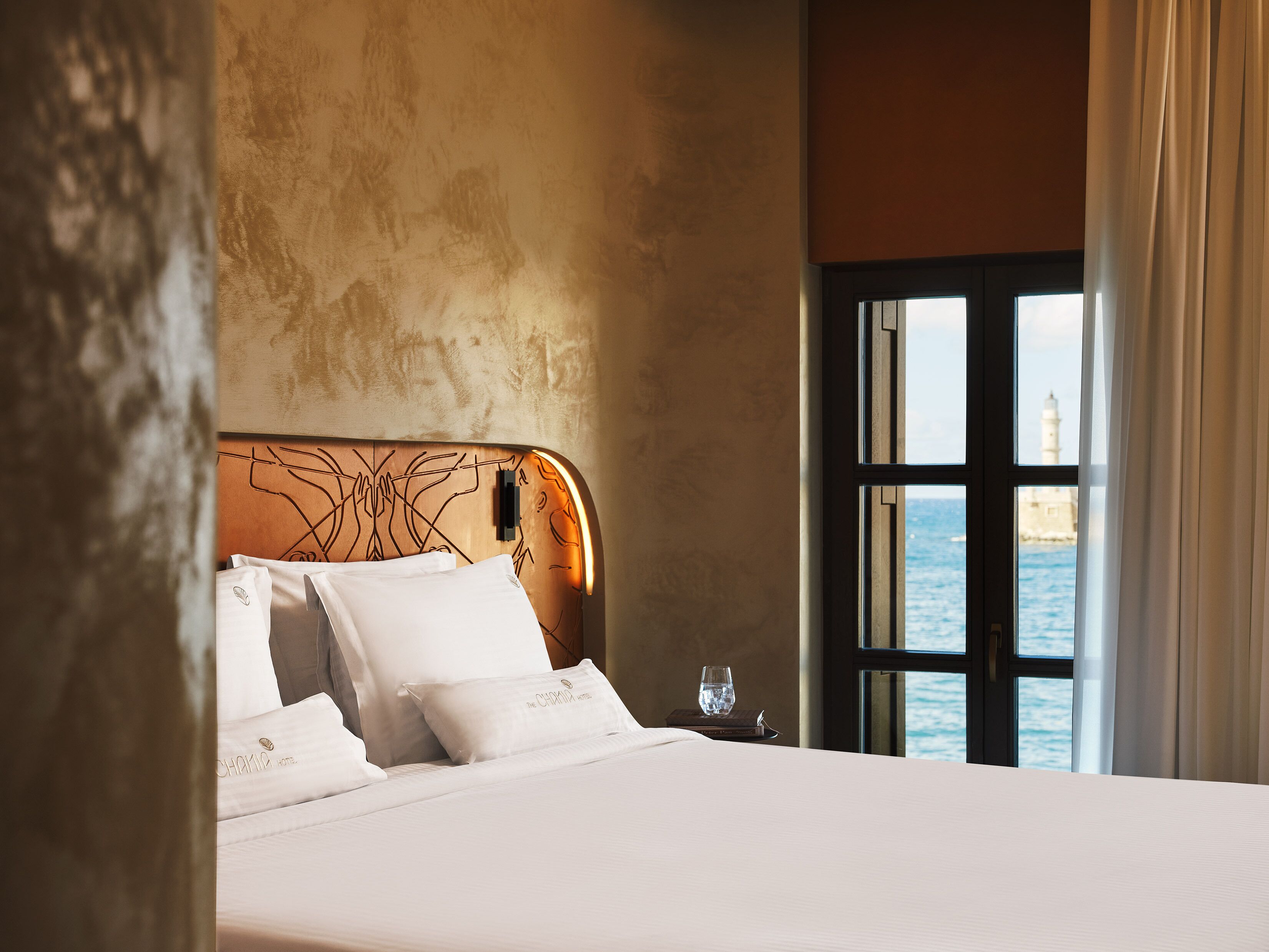 Une chambre d’hôtel avec un grand lit, une vue sur la mer et une fenêtre avec des rideaux.