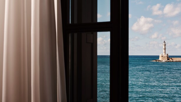A window view of a lighthouse on a rocky outcrop in the sea.
