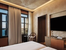 Ein Hotelzimmer mit Bett, Schreibtisch, Stuhl, Fernseher und einem Fenster mit Vorhängen.