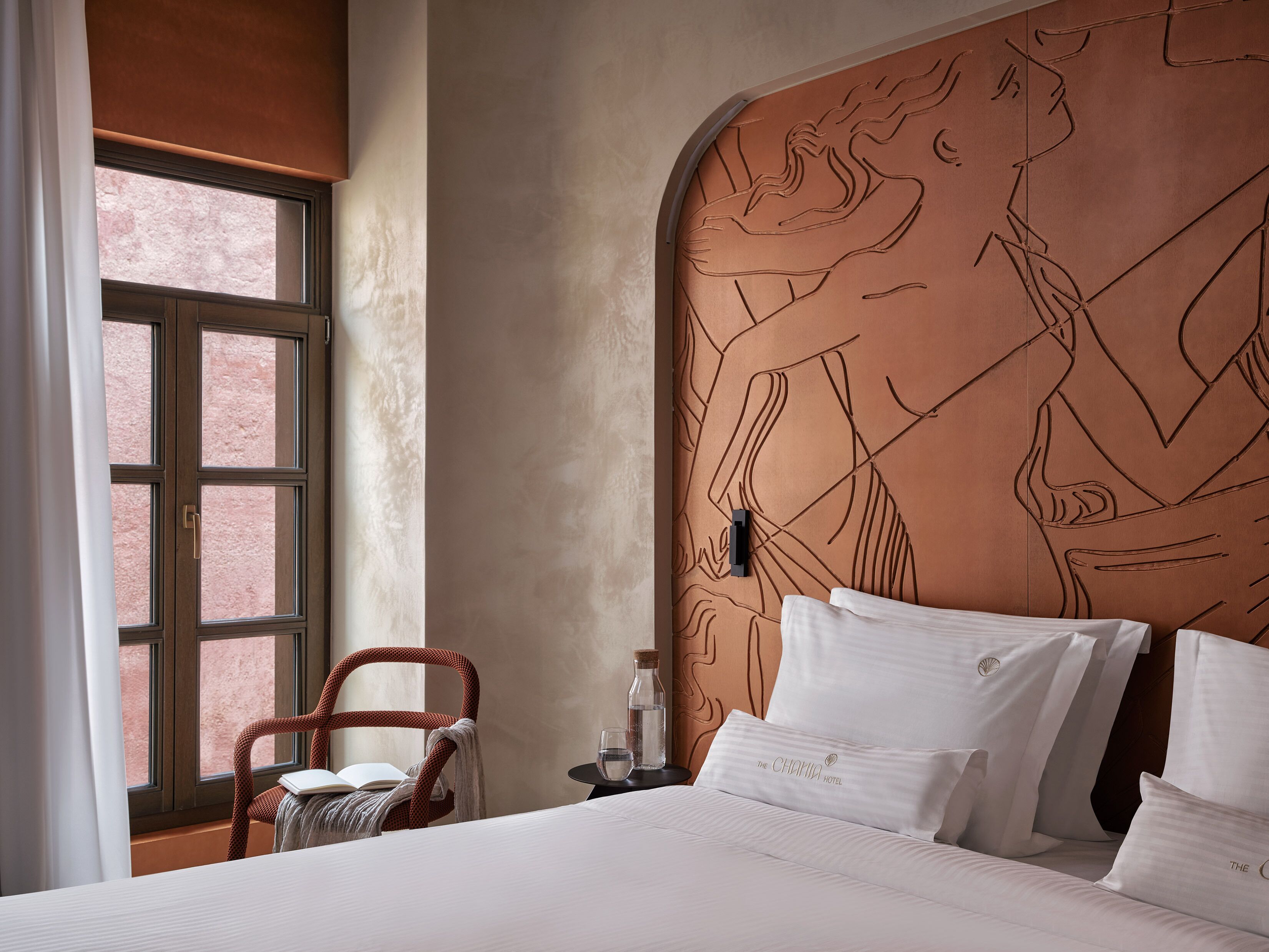 A hotel room with a large bed, a chair, a nightstand, and a wall with a large mural.