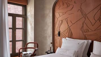 A hotel room with a large bed, a chair, a nightstand, and a wall with a large mural.