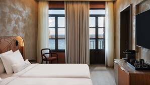 A hotel room with a large bed, a chair, a TV, a coffee maker, and a view of the sea through a window.
