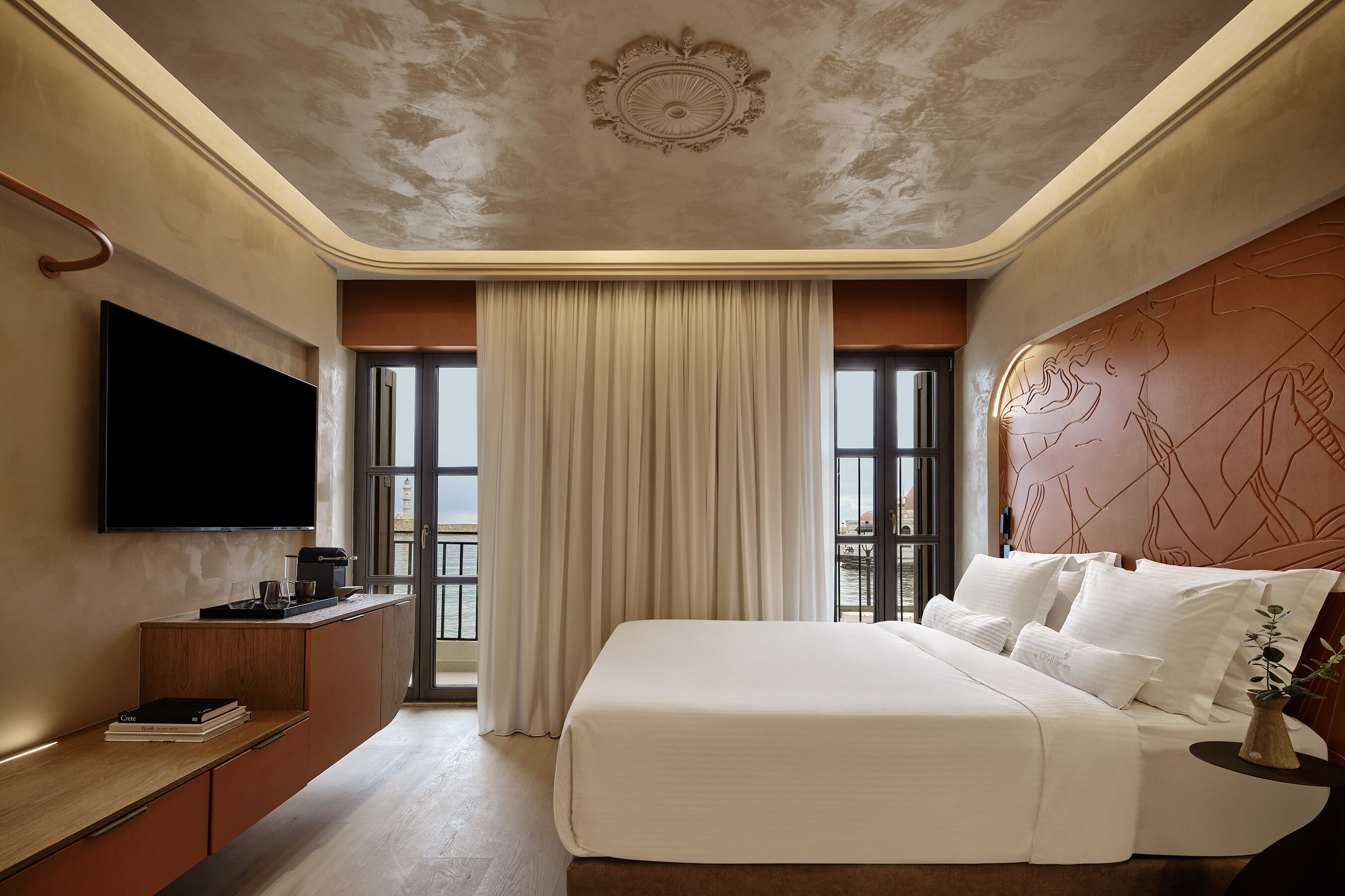 A hotel room with a large bed, a flat-screen TV, a wooden console, and a view of the sea.