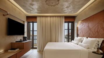 A hotel room with a large bed, a flat-screen TV, a wooden console, and a view of the sea.