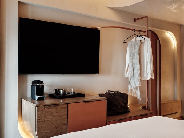 Ein modernes Hotelzimmer mit Flachbildfernseher, Minibar, Bademantel und Holztisch.