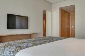 Une chambre d’hôtel moderne dotée d’un grand lit, d’un téléviseur à écran plat fixé au mur et d’une armoire en bois.