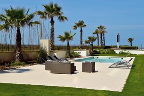 Zona de piscina con sillones de descanso, una piscina y palmeras.