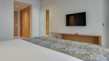 Une chambre à coucher avec un grand lit, un téléviseur fixé au mur et une tête de lit en bois.