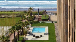 Ein Poolbereich mit Blick auf den Ozean, eine Rasenfläche und eine moderne Gebäudefassade.
