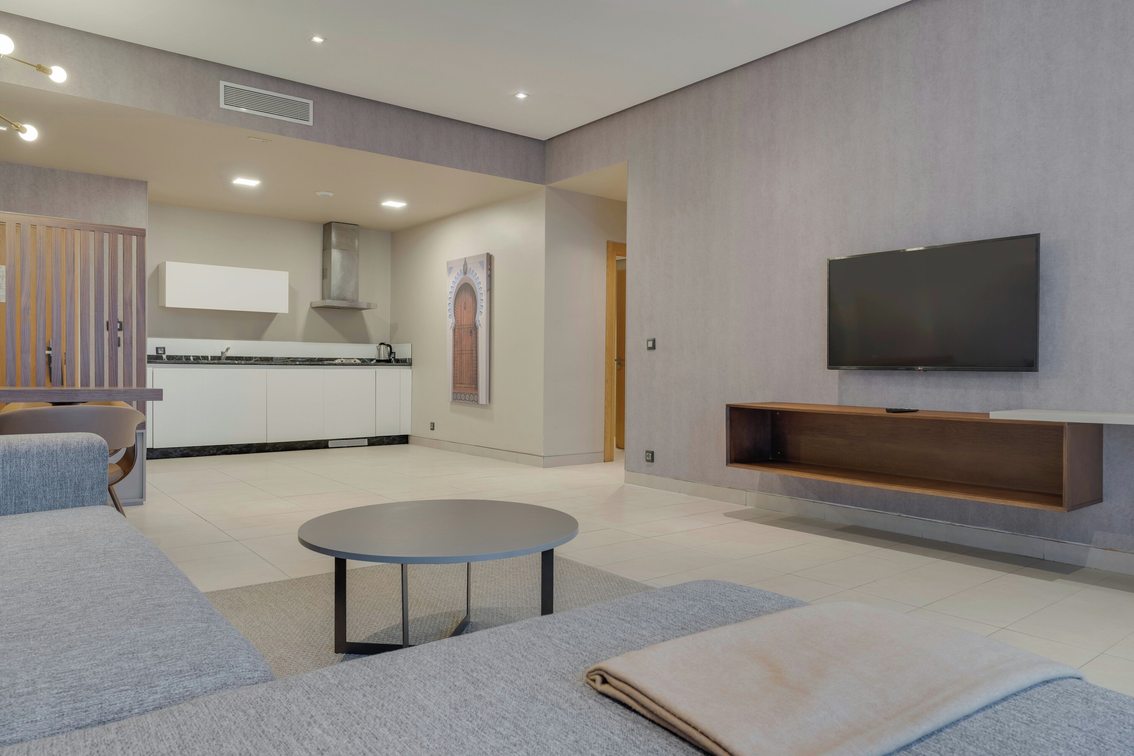 A modern living room with a flat-screen TV, a sofa, a coffee table, and a kitchen area in the background.