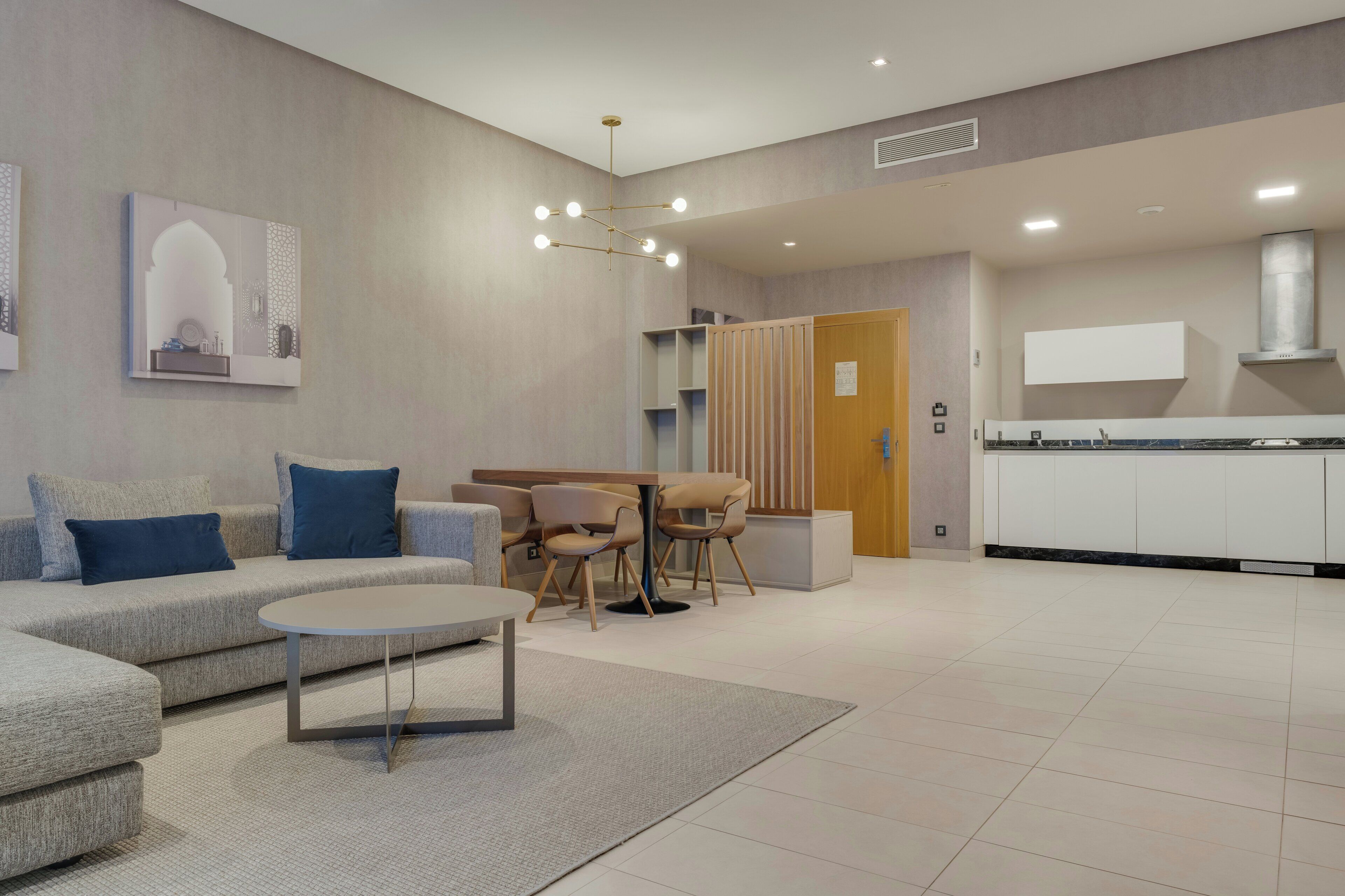 A modern living room with a sofa, coffee table, and chairs. There is a kitchen area with cabinets and a countertop.
