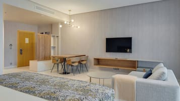Una habitación de hotel moderna con una cama grande, un área de comedor, un televisor y un espacio para sentarse.