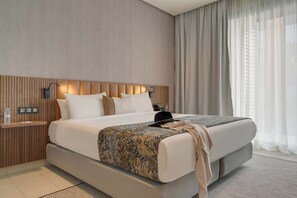Een moderne hotelkamer met een groot bed, een houten hoofdbord, een nachtkastje met een lamp en dunne gordijnen.