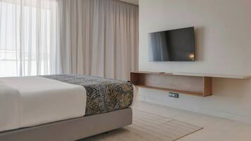 A modern hotel room with a bed, a flat-screen TV mounted on the wall, and a wooden shelf below it.