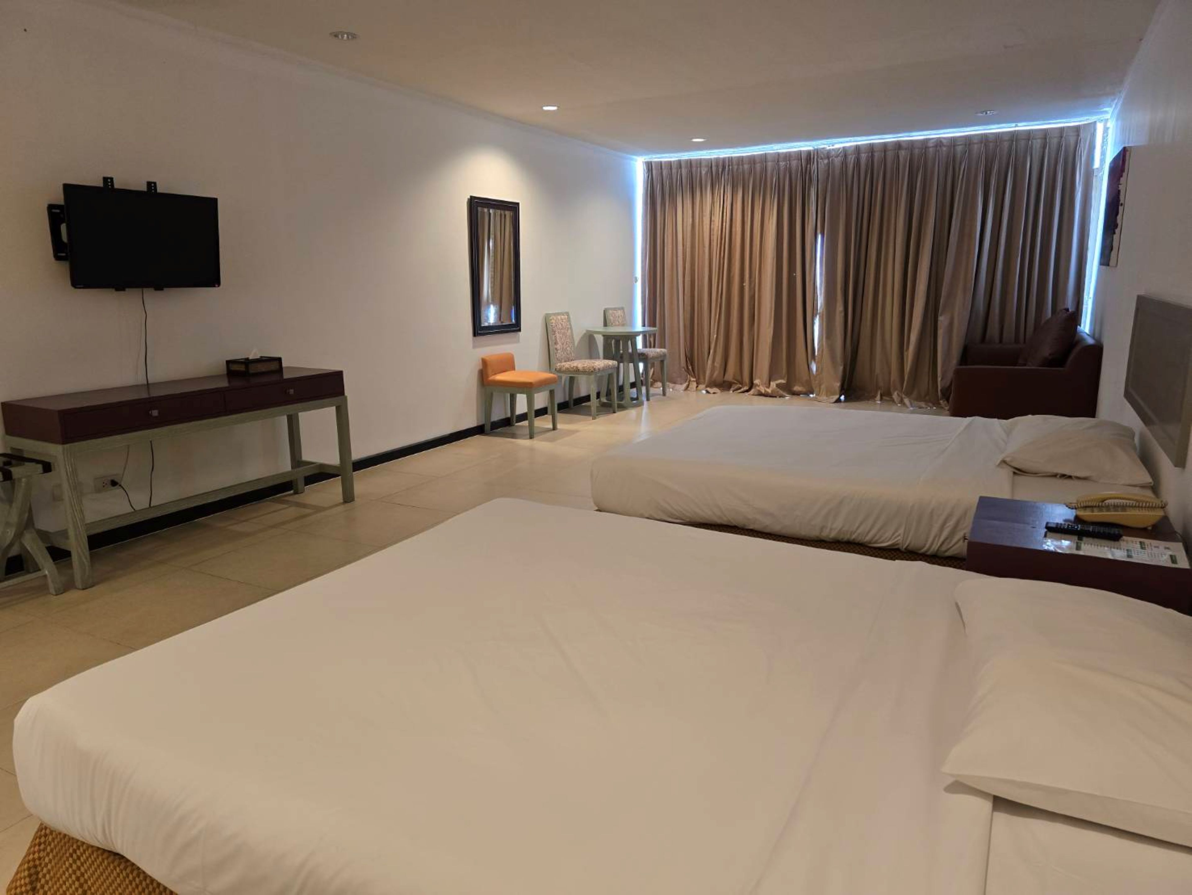A hotel room with two beds, a desk, a TV, and a window with curtains.