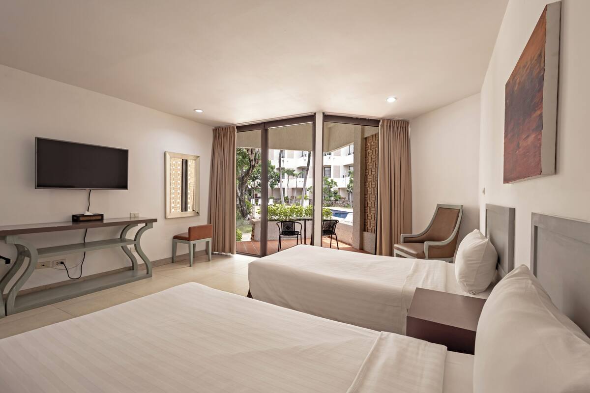 A hotel room with two beds, a TV, a desk, and a balcony with a view.