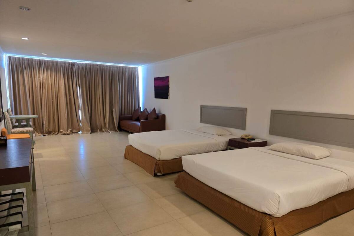 A hotel room with two beds, a desk, a sofa, and a large window with curtains.