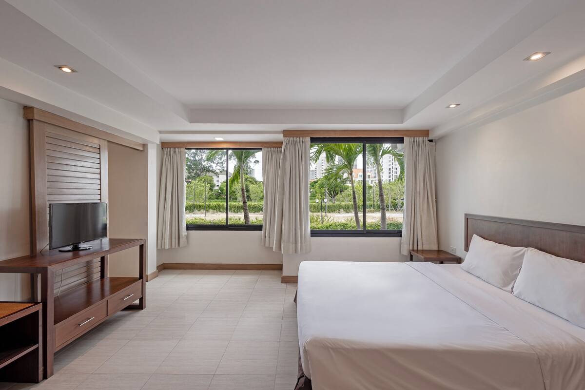 A hotel room with a bed, TV, and windows with curtains.