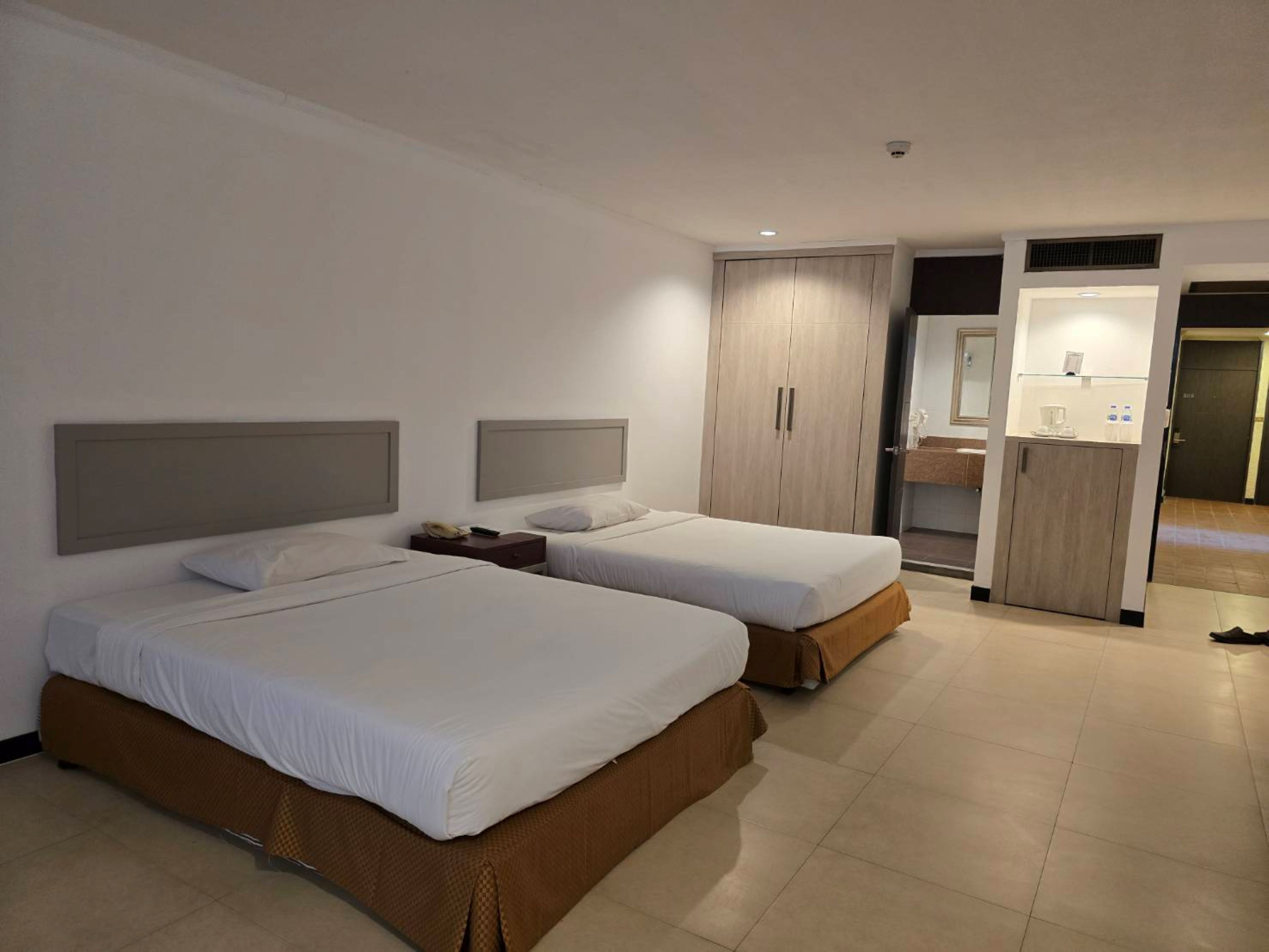 Een hotelkamer met twee bedden, een kledingkast, een badkamer met een spiegel en een wastafel.