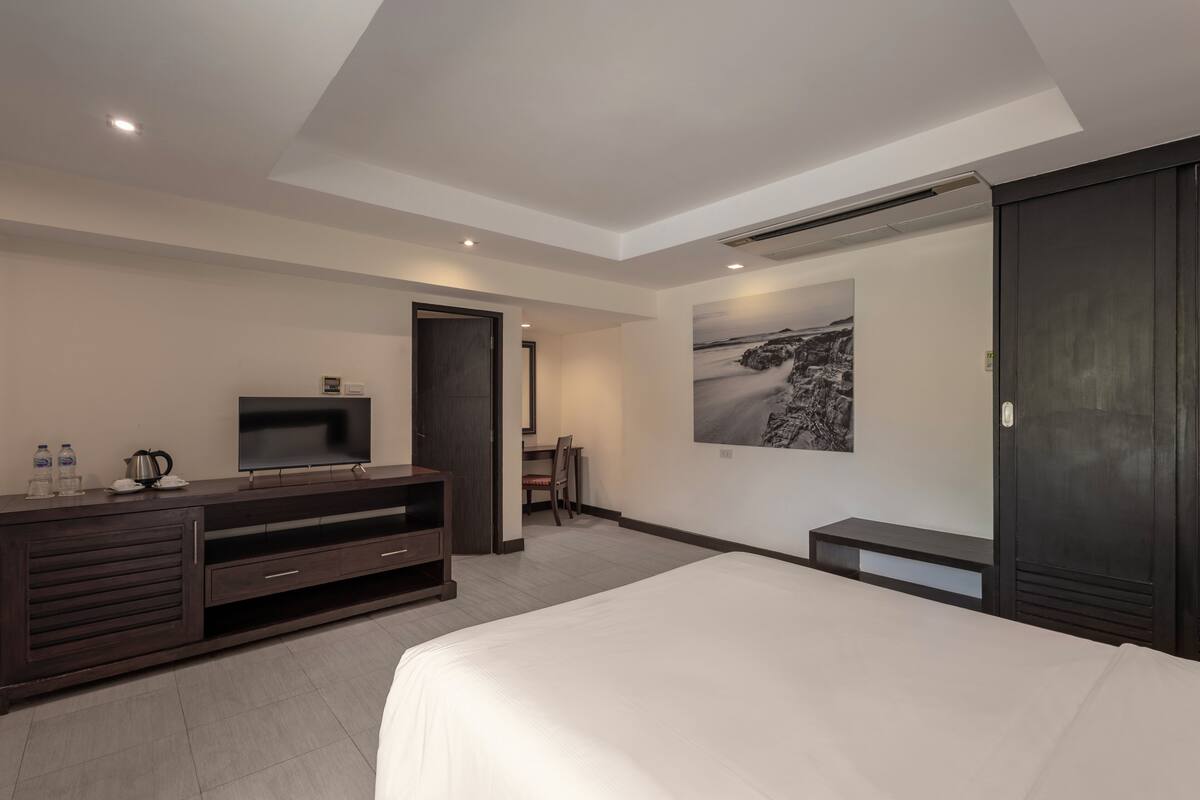 A modern hotel room with a large bed, a flat-screen TV, a dark wooden dresser, and a painting on the wall.