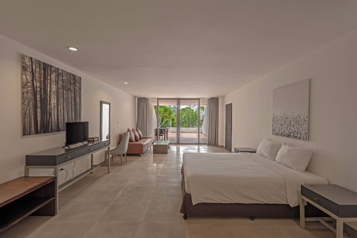 A modern bedroom with a large bed, a TV, a desk, and a balcony with curtains.