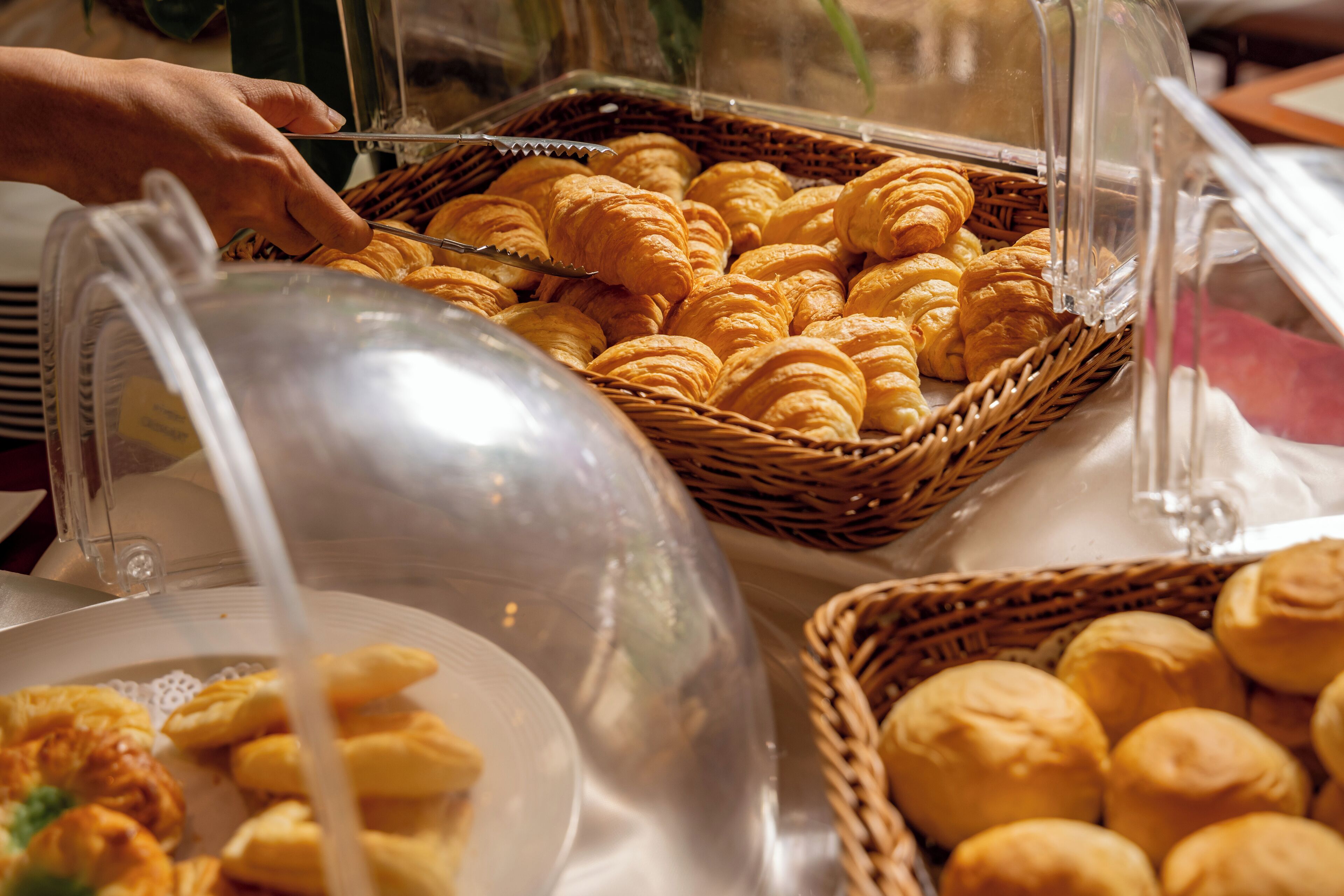 A buffet with various baked goods, including croissants and rolls, in wicker baskets.