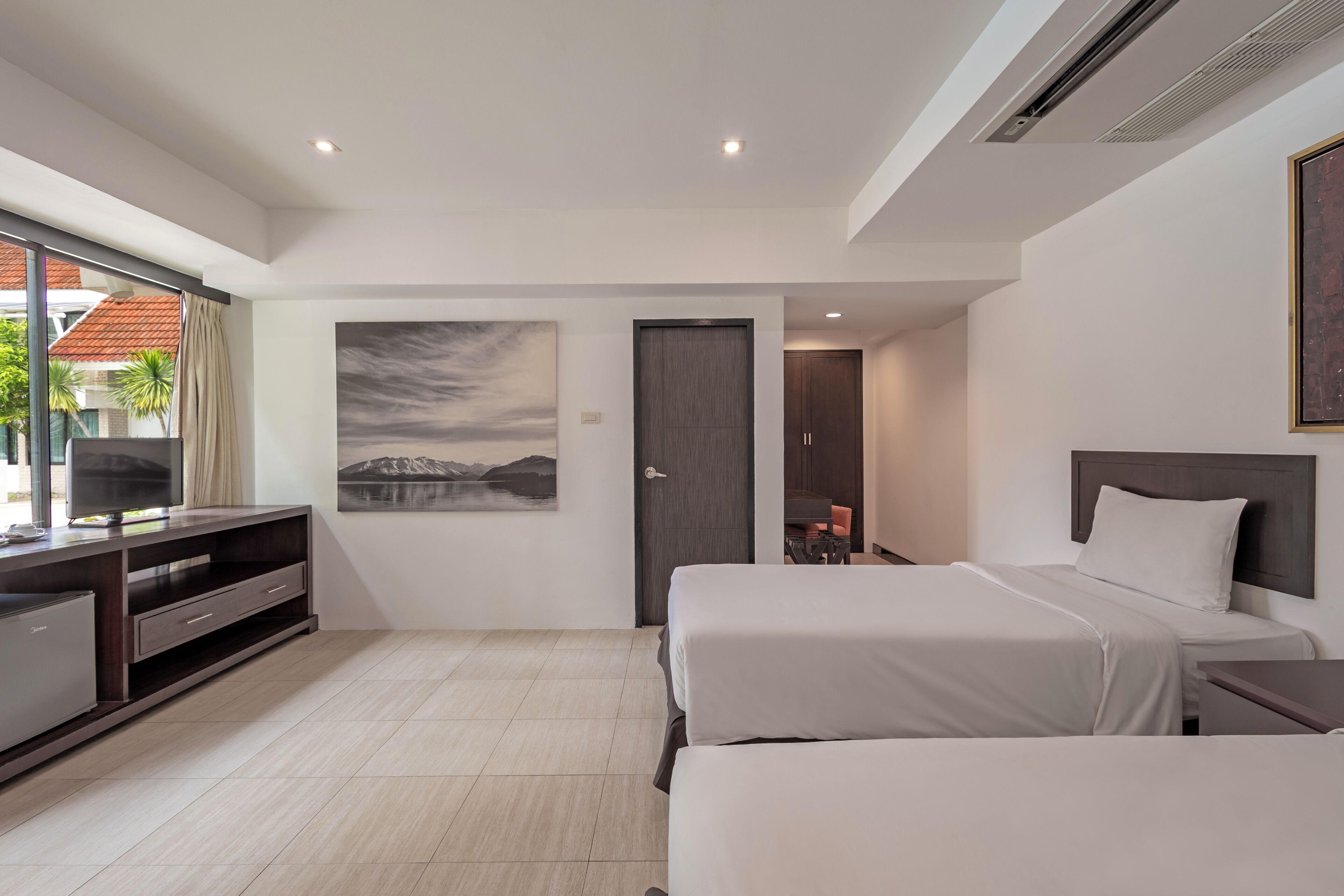 Et moderne hotelværelse med to senge, et fjernsyn, et skrivebord og et billede på væggen.