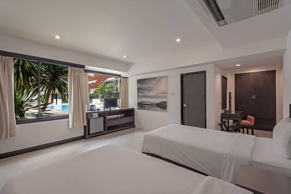 A modern hotel room with two beds, a desk, a chair, and a large window with curtains.