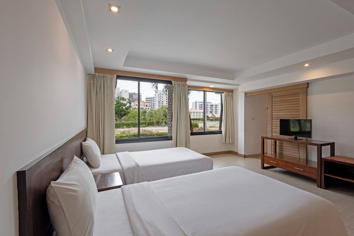 A hotel room with two beds, a TV on a wooden console, and a large window with curtains.