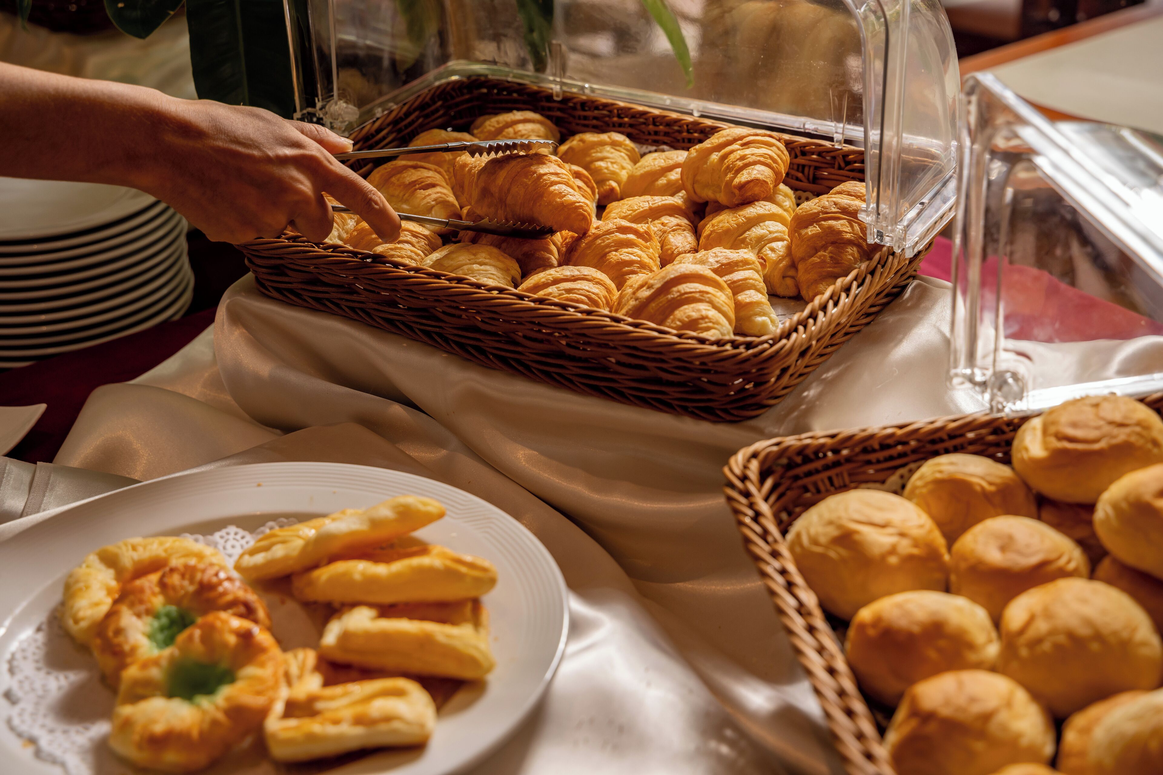 Un bufé con diversas opciones de panadería, como cruasanes y panecillos, presentados en cestas y platos.