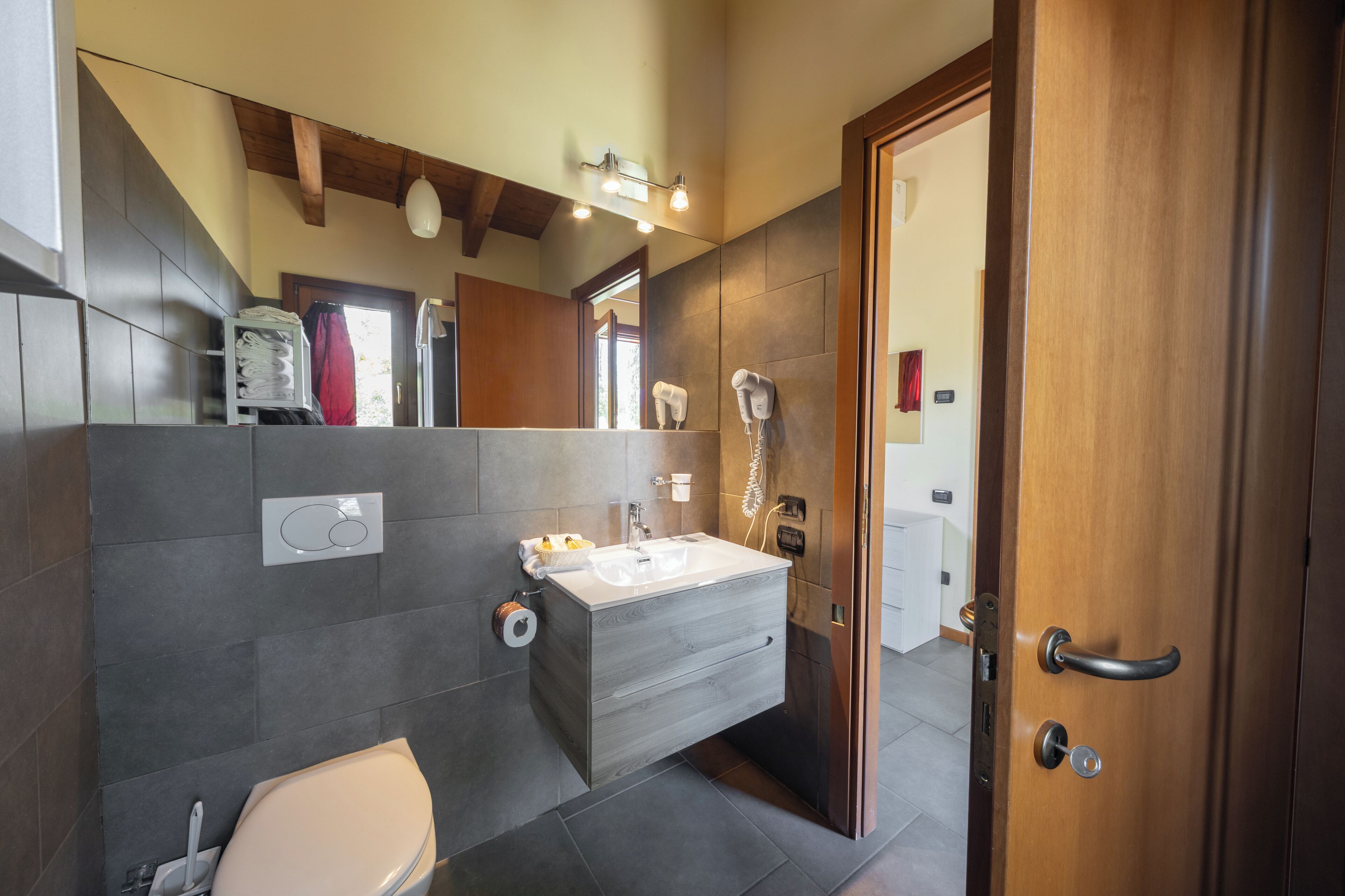 A modern bathroom with a large mirror, a built-in sink, a toilet, and a shower area.
