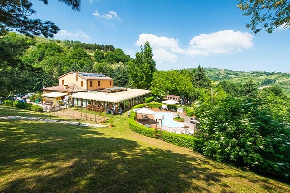 A villa with a large patio, surrounded by lush greenery and hills. - La Valle Dei Caprioli - B&B (Montescudo)