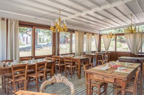 A restaurant with wooden tables and chairs, large windows, and chandeliers. - La Valle Dei Caprioli - B&B (Montescudo)