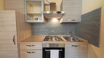 A modern kitchen with a built-in stove, sink, and oven. There are wooden cabinets and a marble backsplash.