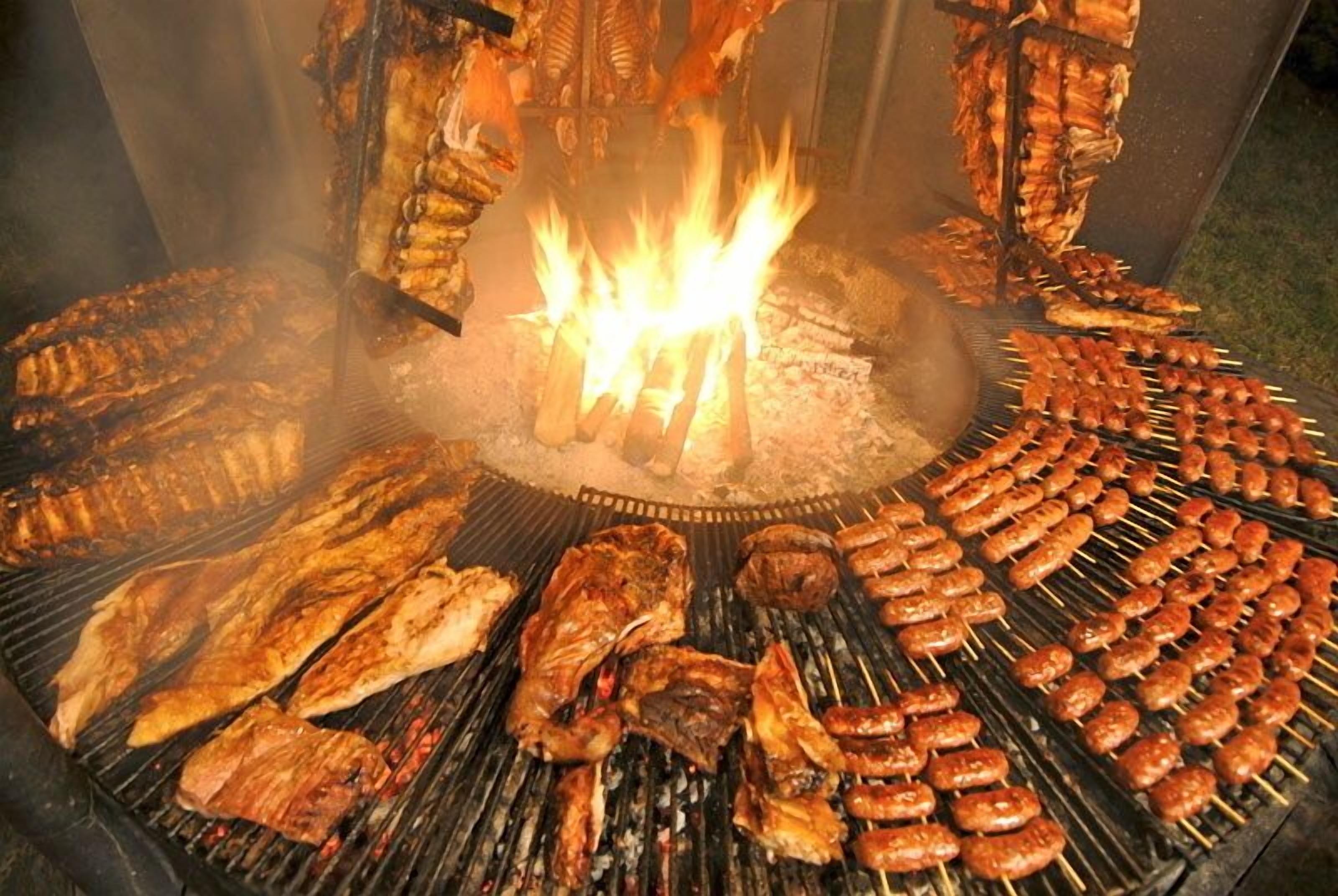 A large outdoor grill with various meats and sausages being cooked over an open fire.