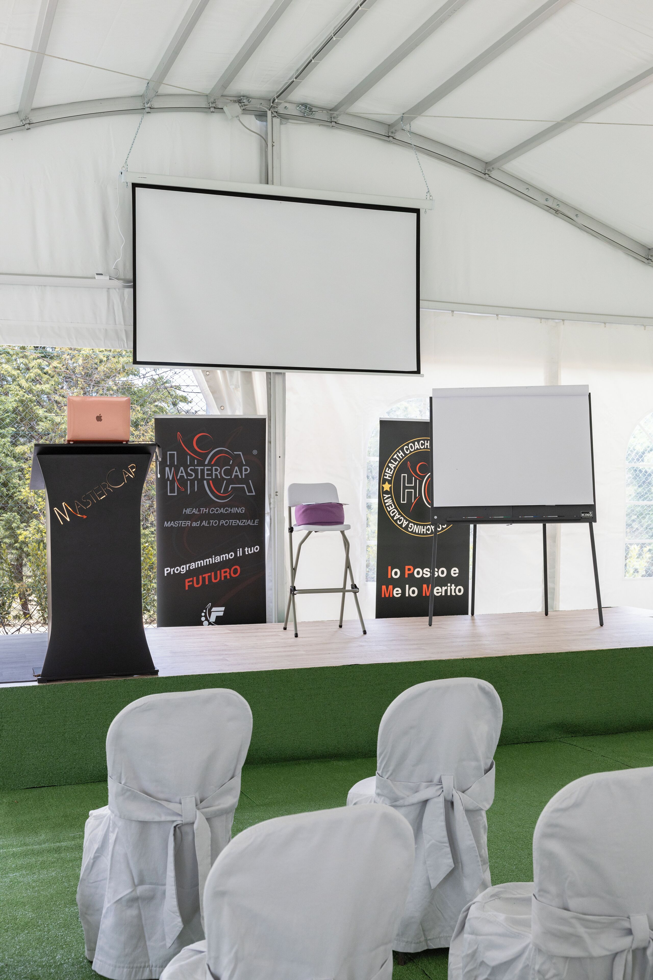 An indoor event space with a stage, two podiums, a laptop, and chairs.