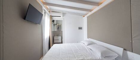 A hotel room with a bed, a TV mounted on the wall, and a bathroom visible through an open door.
