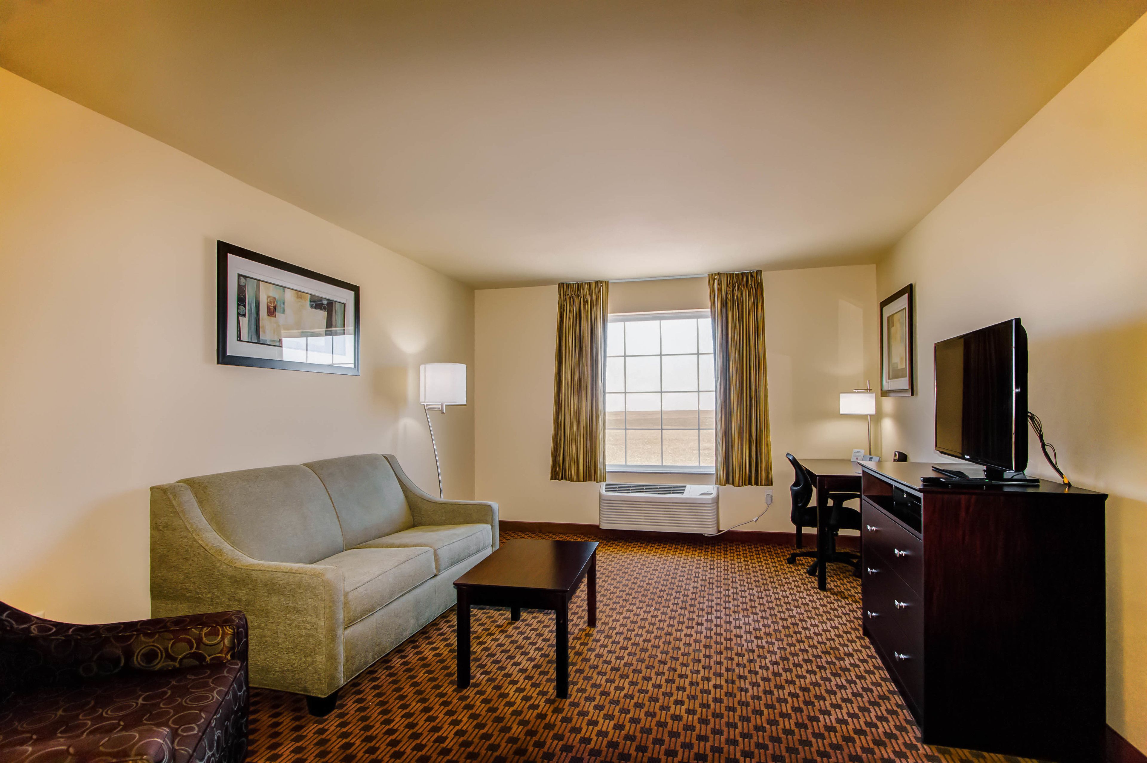 A hotel room with a sofa, a desk, a television, and a patterned carpet.