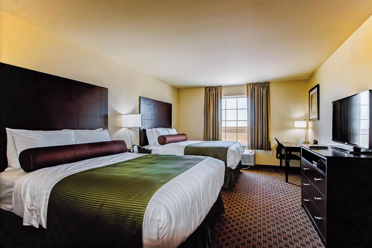 A hotel room with two beds, a desk, a television, and a window with curtains.